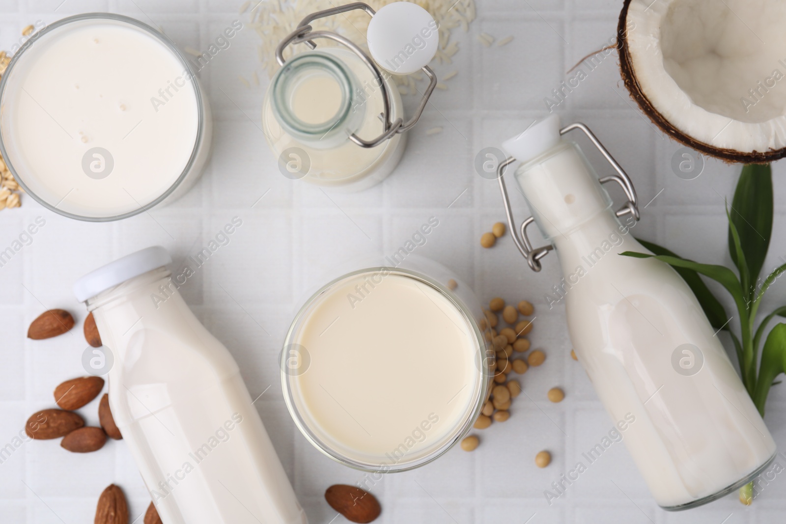 Photo of Different types of vegan milk and ingredients on white tiled table, flat lay