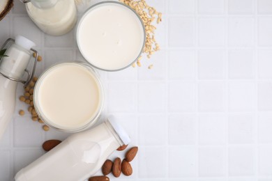 Photo of Different types of vegan milk and ingredients on white tiled table, flat lay. Space for text