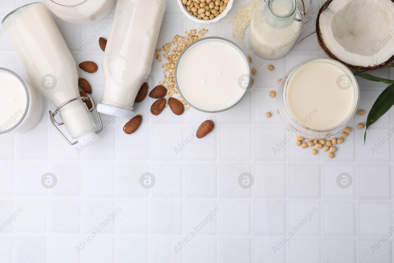 Photo of Different types of vegan milk and ingredients on white tiled table, flat lay. Space for text