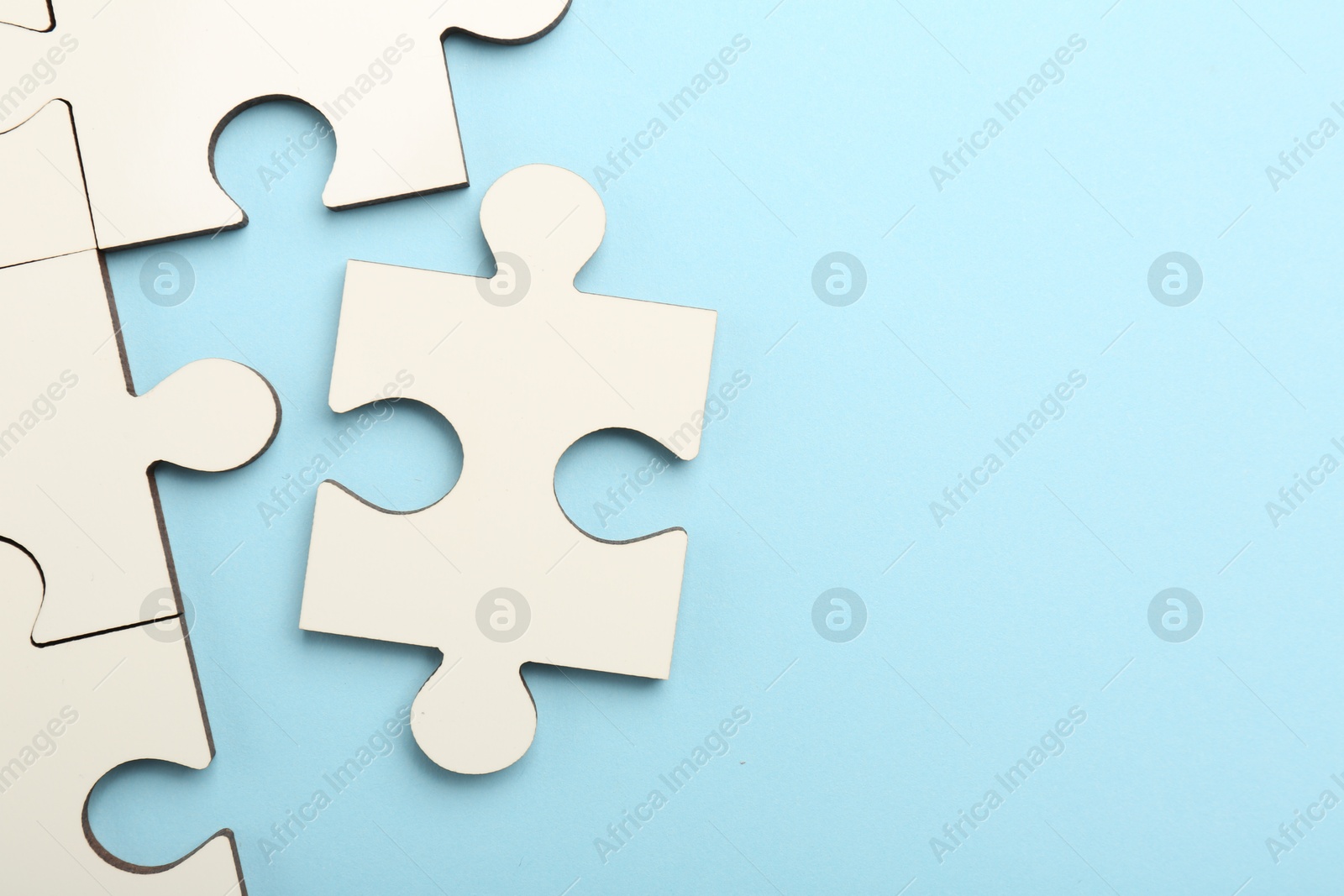 Photo of White puzzle pieces on light blue background, top view. Space for text