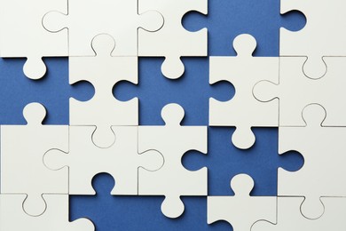 White puzzle with missing pieces on blue background, top view