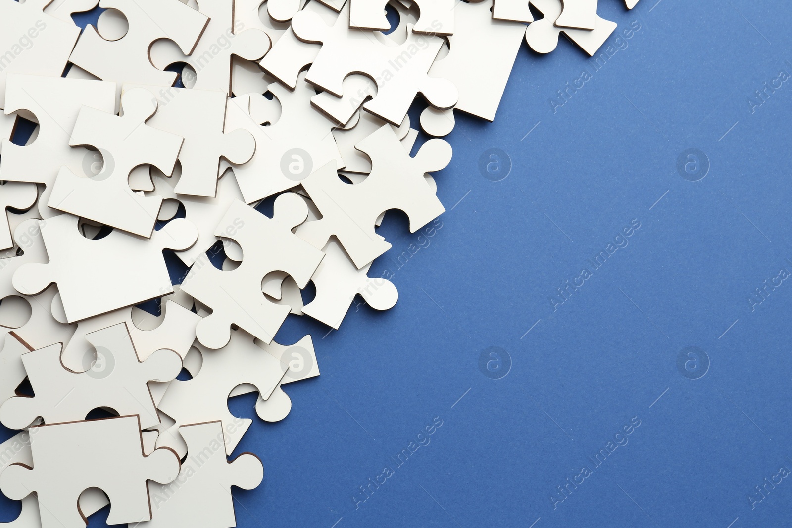 Photo of White puzzle pieces on blue background, top view. Space for text