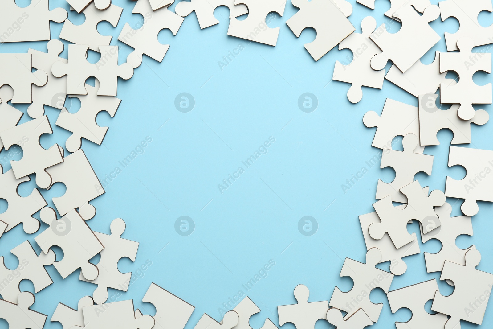 Photo of Frame of white puzzle pieces on light blue background, top view. Space for text