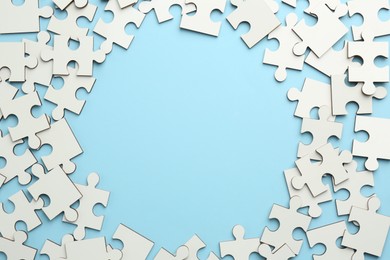 Photo of Frame of white puzzle pieces on light blue background, top view. Space for text