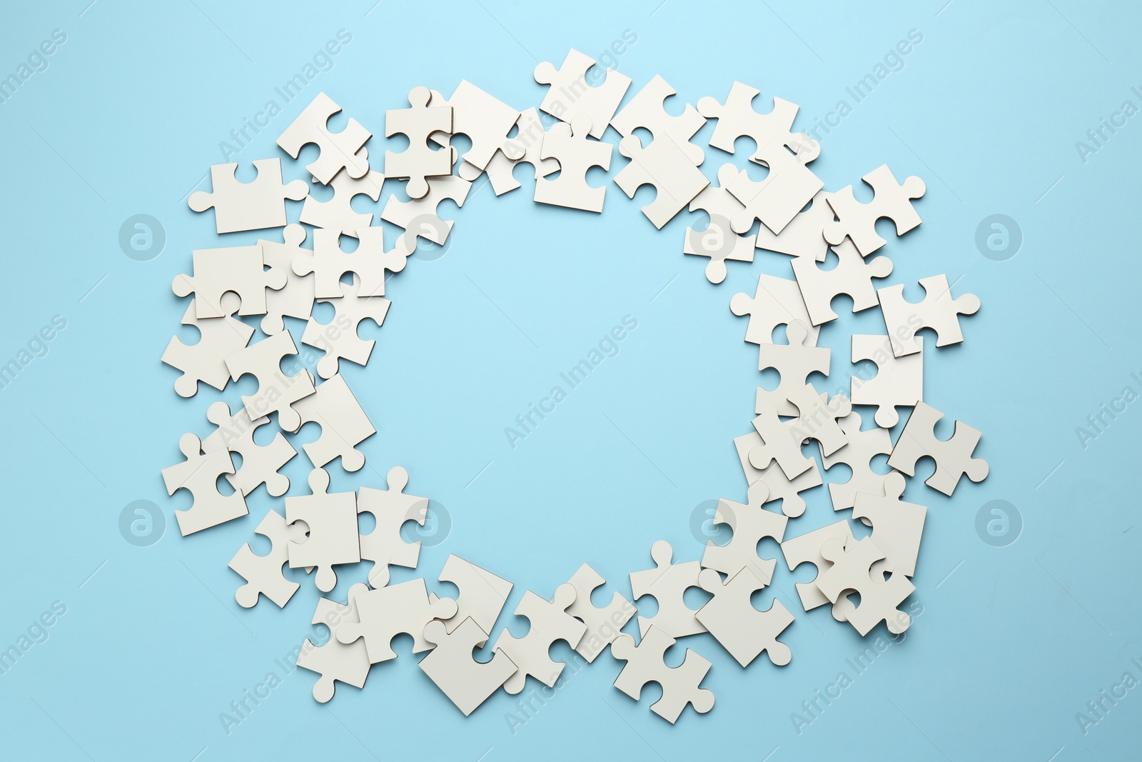 Photo of Frame of white puzzle pieces on light blue background, top view. Space for text