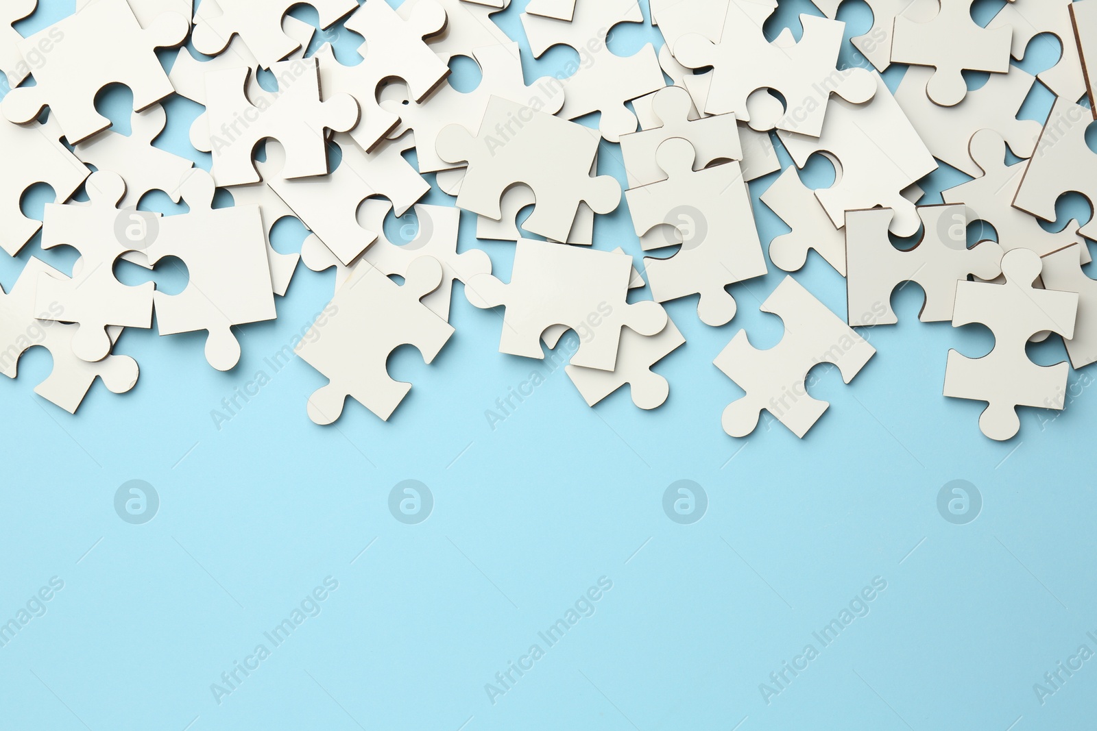 Photo of White puzzle pieces on light blue background, top view. Space for text