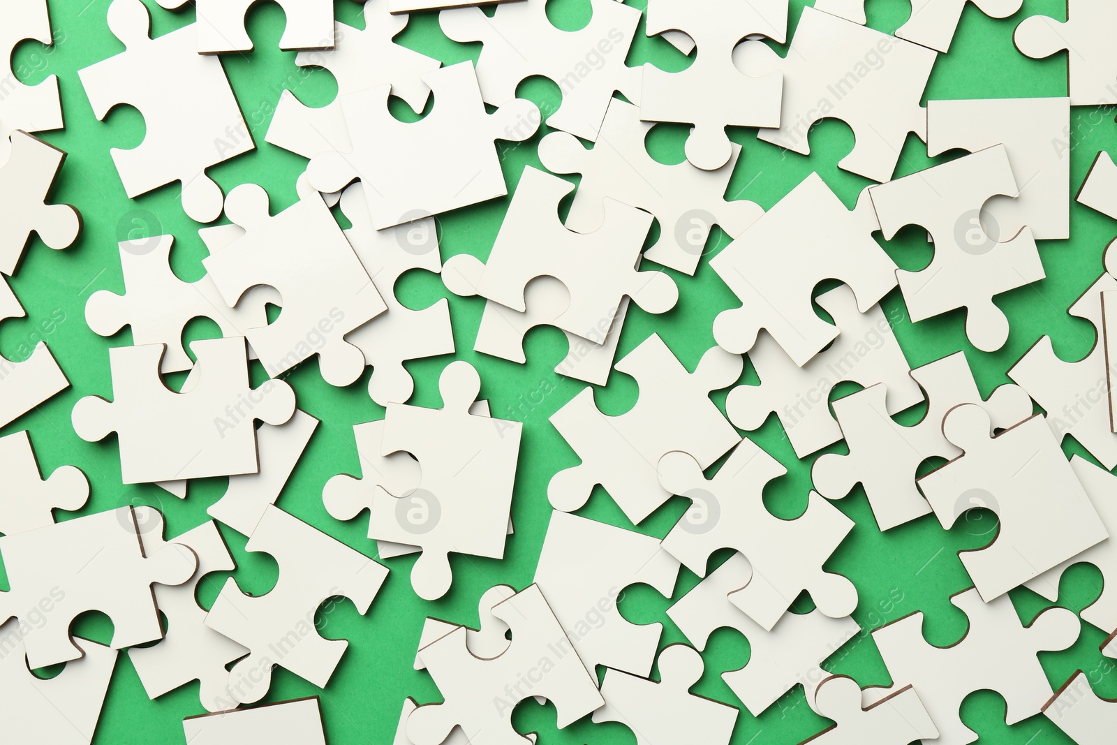 Photo of White puzzle pieces on green background, top view