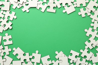 Photo of Frame of white puzzle pieces on green background, top view. Space for text