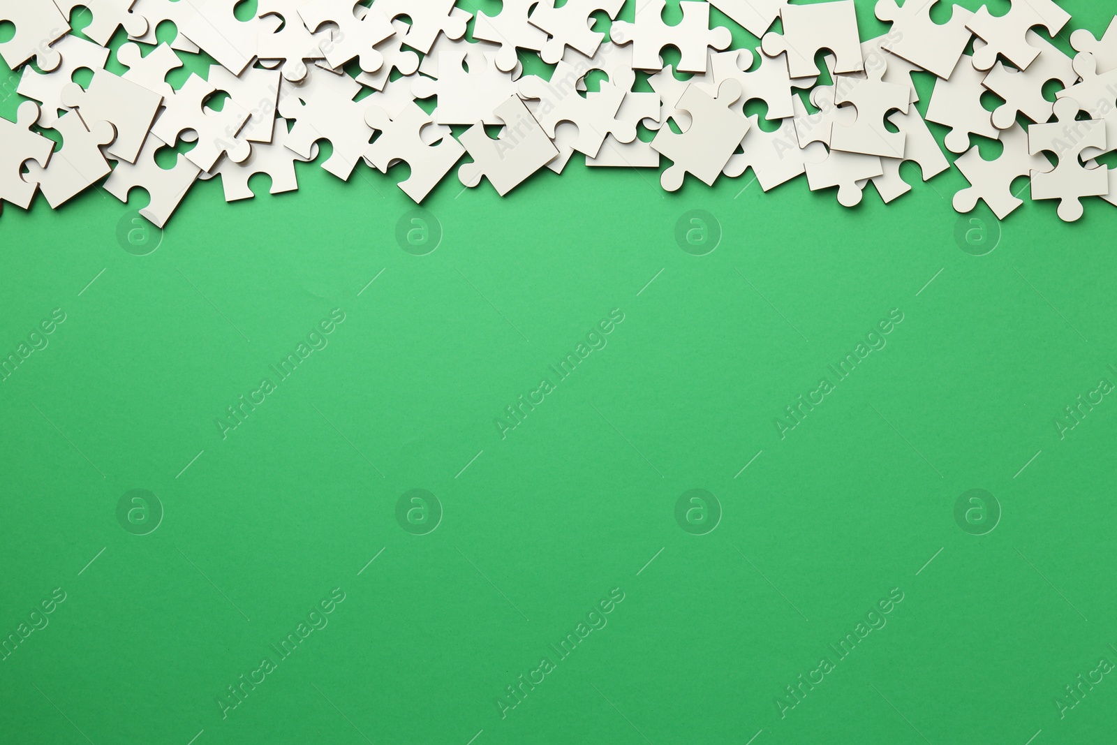 Photo of White puzzle pieces on green background, top view. Space for text