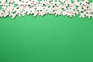 Photo of White puzzle pieces on green background, top view. Space for text