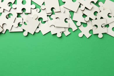 Photo of White puzzle pieces on green background, top view. Space for text