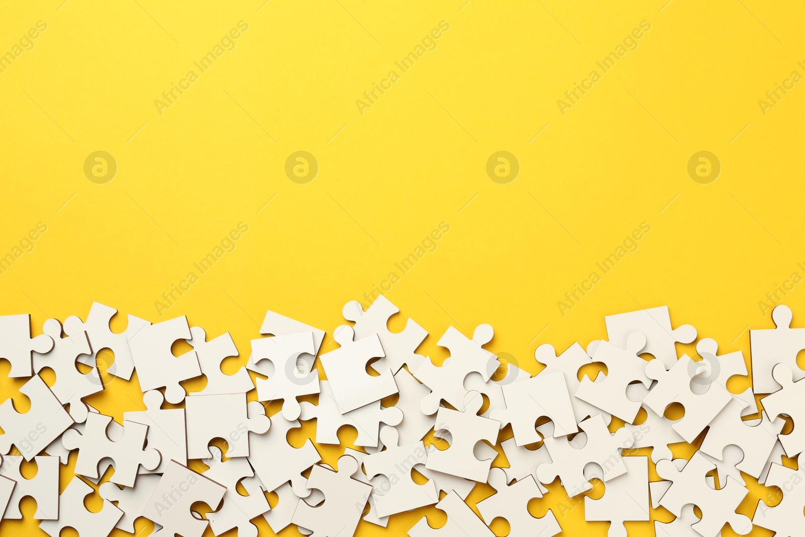 Photo of White puzzle pieces on yellow background, top view. Space for text