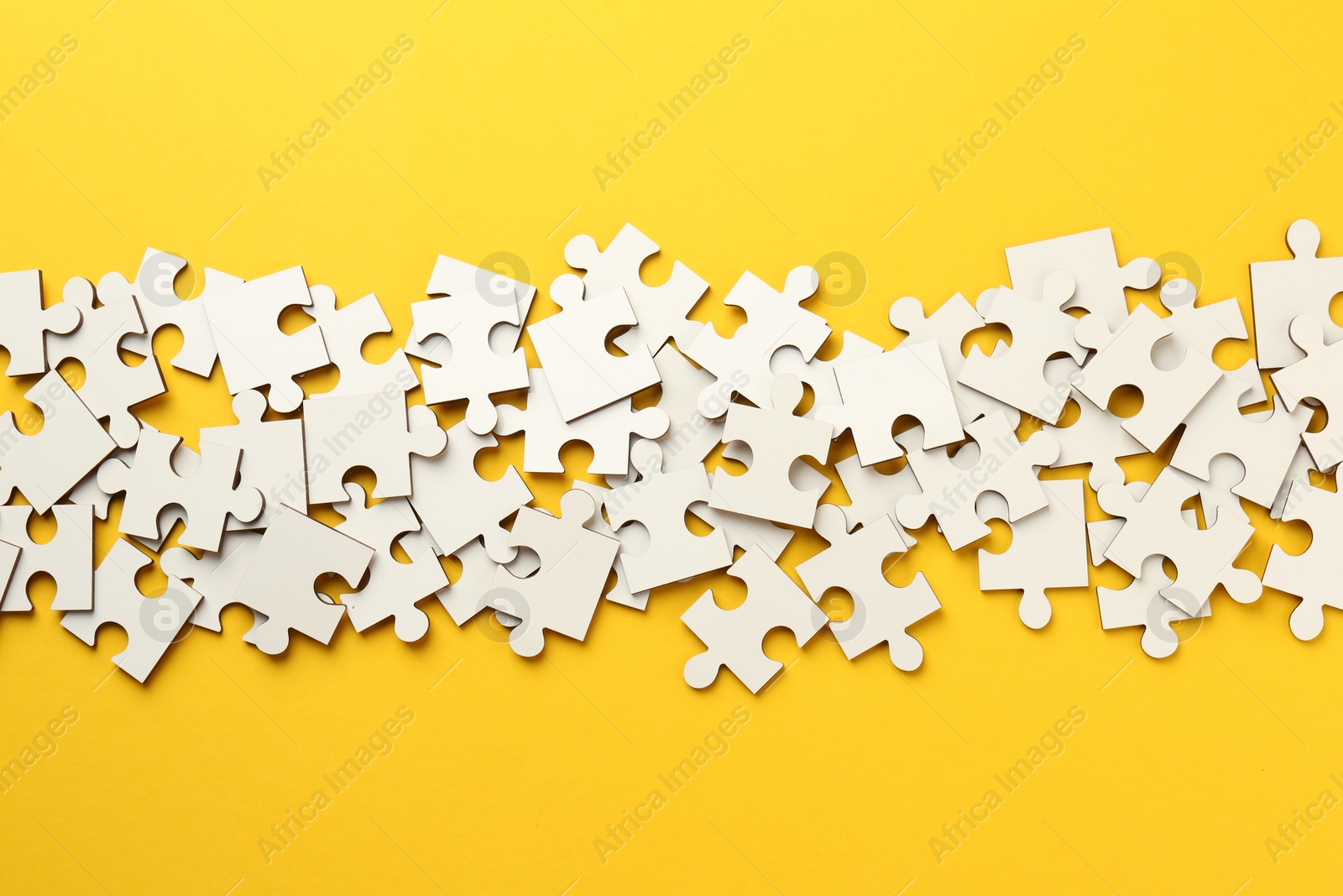 Photo of White puzzle pieces on yellow background, top view