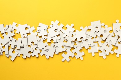 Photo of White puzzle pieces on yellow background, top view