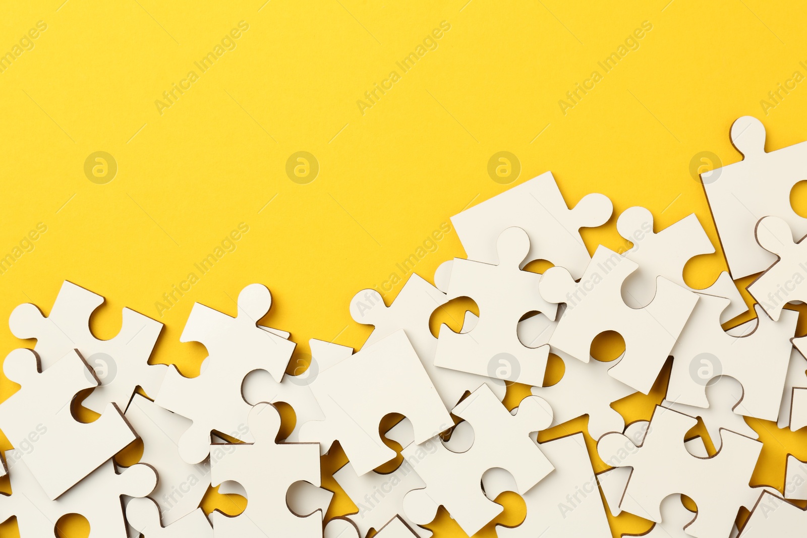 Photo of White puzzle pieces on yellow background, top view. Space for text