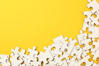 Photo of White puzzle pieces on yellow background, top view. Space for text