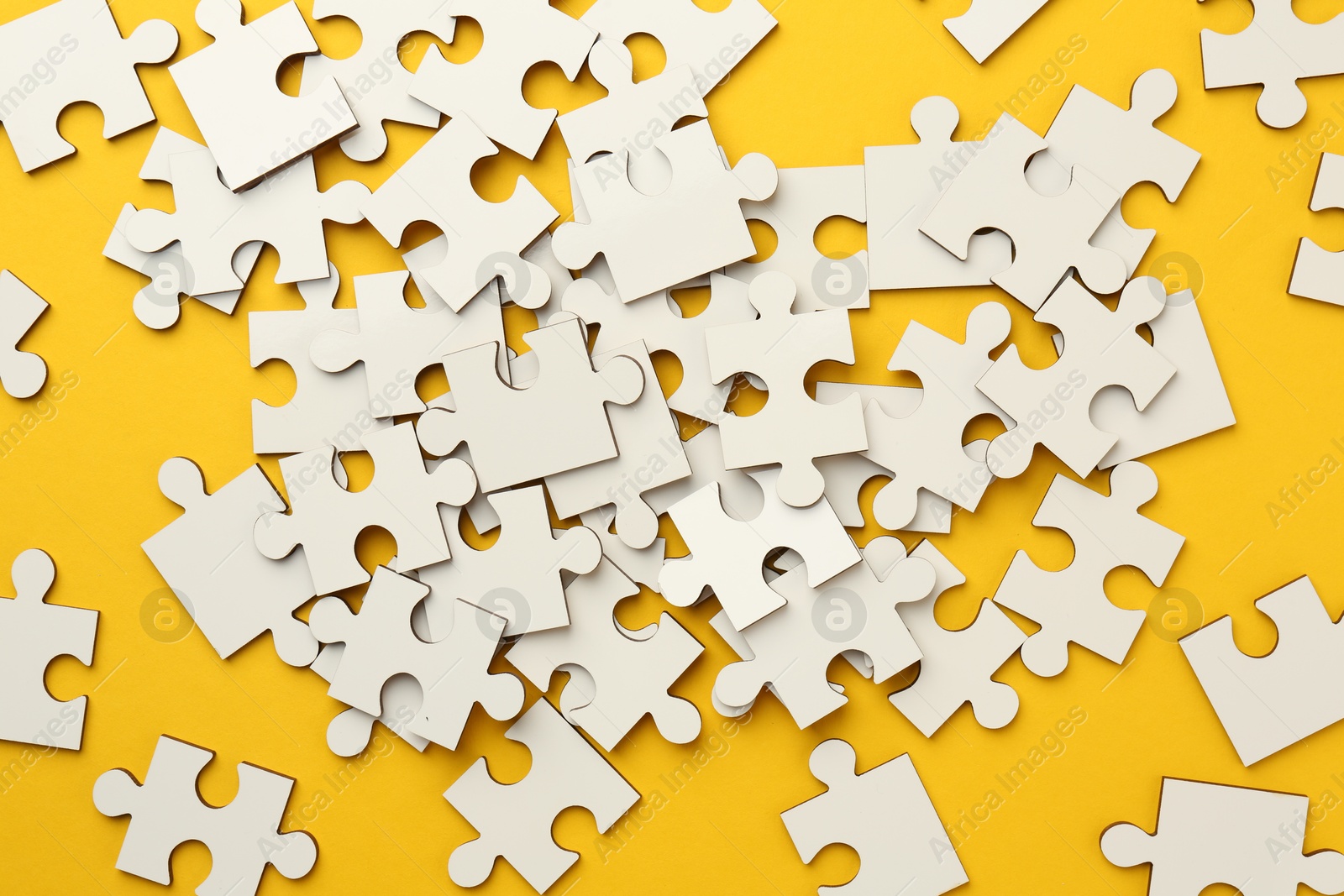 Photo of White puzzle pieces on yellow background, top view