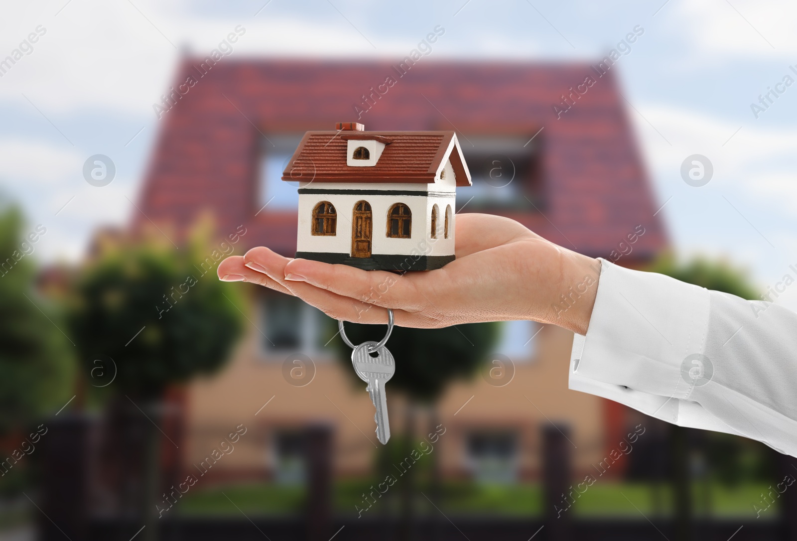 Image of Real estate agent holding house model and key against future dwelling, closeup