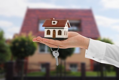 Image of Real estate agent holding house model and key against future dwelling, closeup