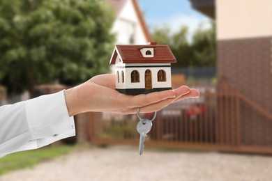 Image of Real estate agent holding house model and key against future dwelling, closeup