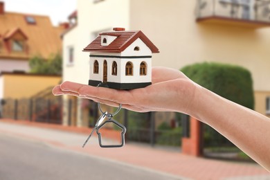 Image of Real estate agent holding house model and key against future dwelling, closeup