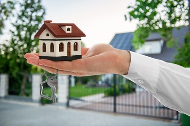 Image of Real estate agent holding house model and key against future dwelling, closeup