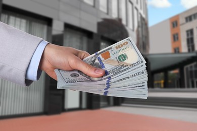 Image of Woman holding money against building, closeup. Real estate purchase