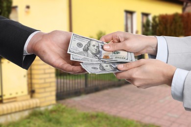 Image of Client giving money to real estate agent against beautiful house, closeup