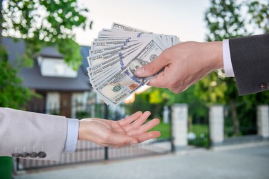 Image of Client giving money to real estate agent against beautiful house, closeup