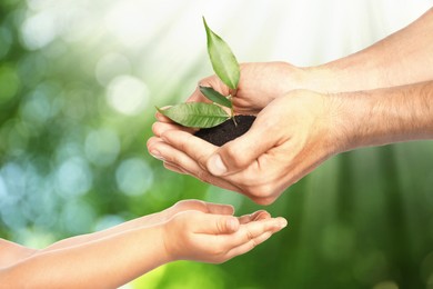 Image of Man passing soil with green plant to his child against blurred background. Environment protection