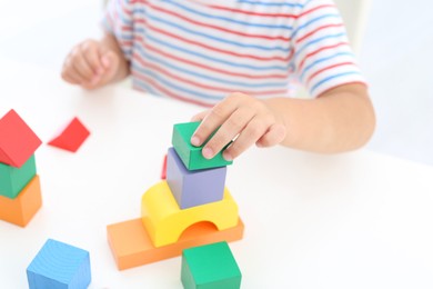 Little boy playing with colorful blocks at white table, closeup. Educational toy