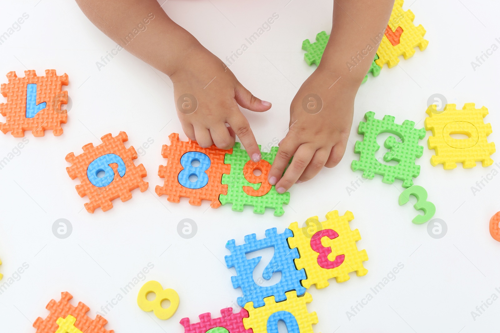 Photo of Little girl playing with colorful puzzles at white table, top view. Educational toy