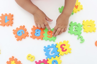 Little girl playing with colorful puzzles at white table, top view. Educational toy