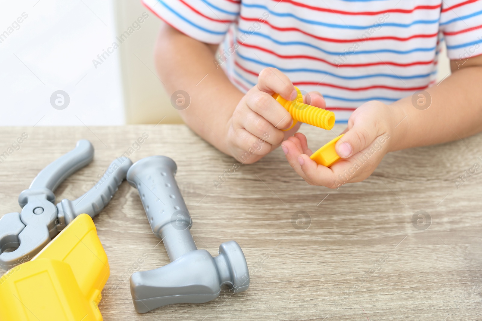 Photo of Little boy playing with toy construction tools at wooden table, closeup