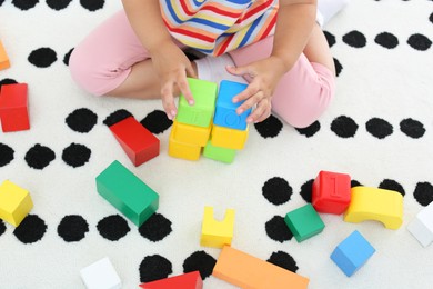 Photo of Cute little girl playing with colorful cubes on floor indoors, above view. Educational toy