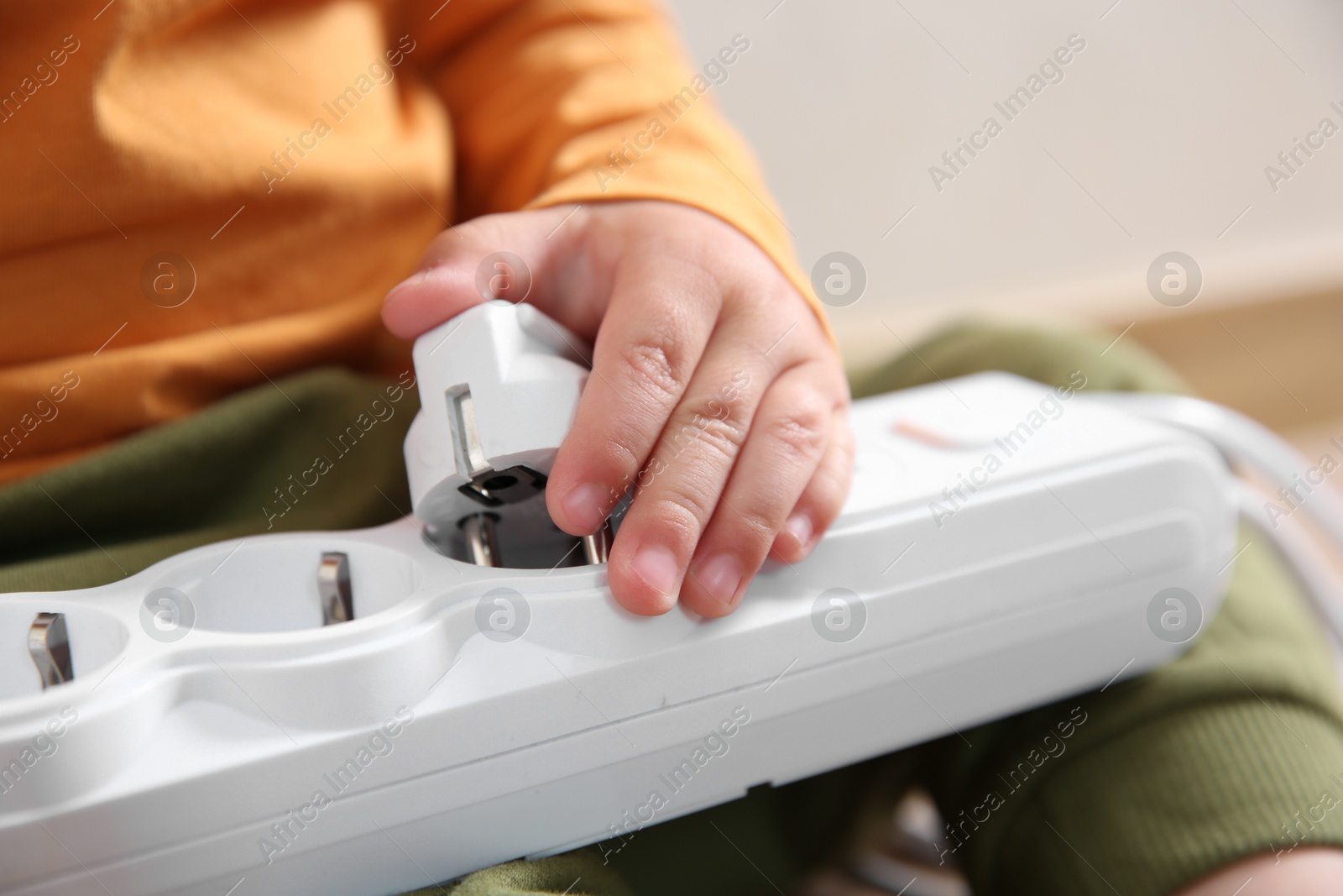 Photo of Little child playing with power strip and plug indoors, closeup