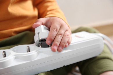 Photo of Little child playing with power strip and plug indoors, closeup