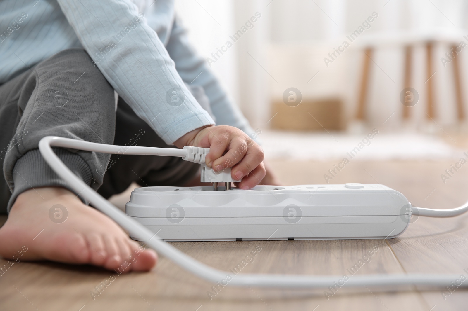 Photo of Little child playing with power strip and plug on floor indoors, closeup. Dangerous situation