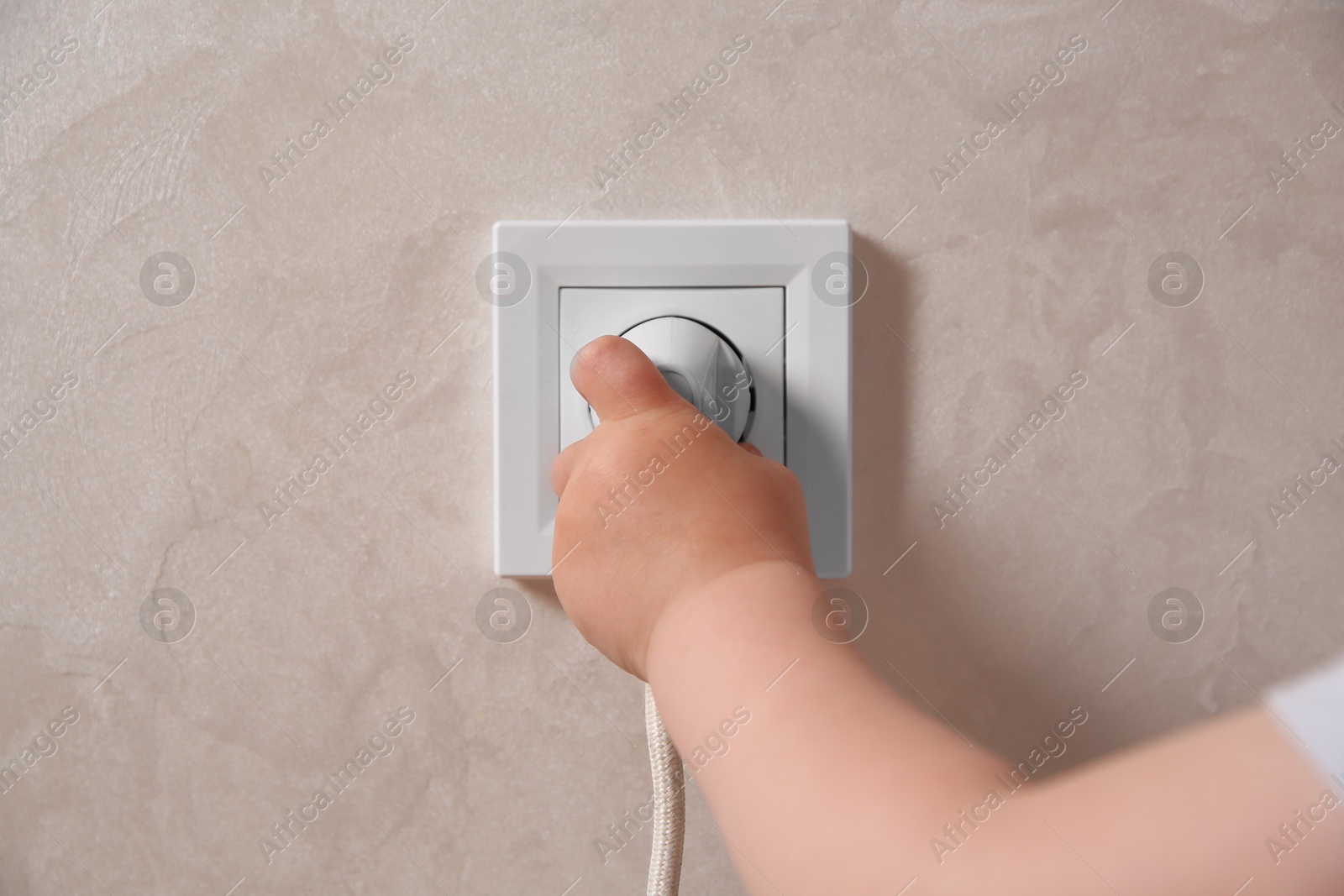 Photo of Little child playing with electrical socket and plug indoors, closeup. Dangerous situation