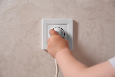 Photo of Little child playing with electrical socket and plug indoors, closeup. Dangerous situation