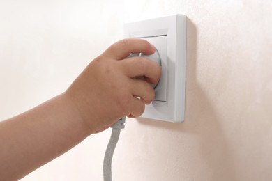 Photo of Little child playing with electrical socket and plug indoors, closeup. Dangerous situation