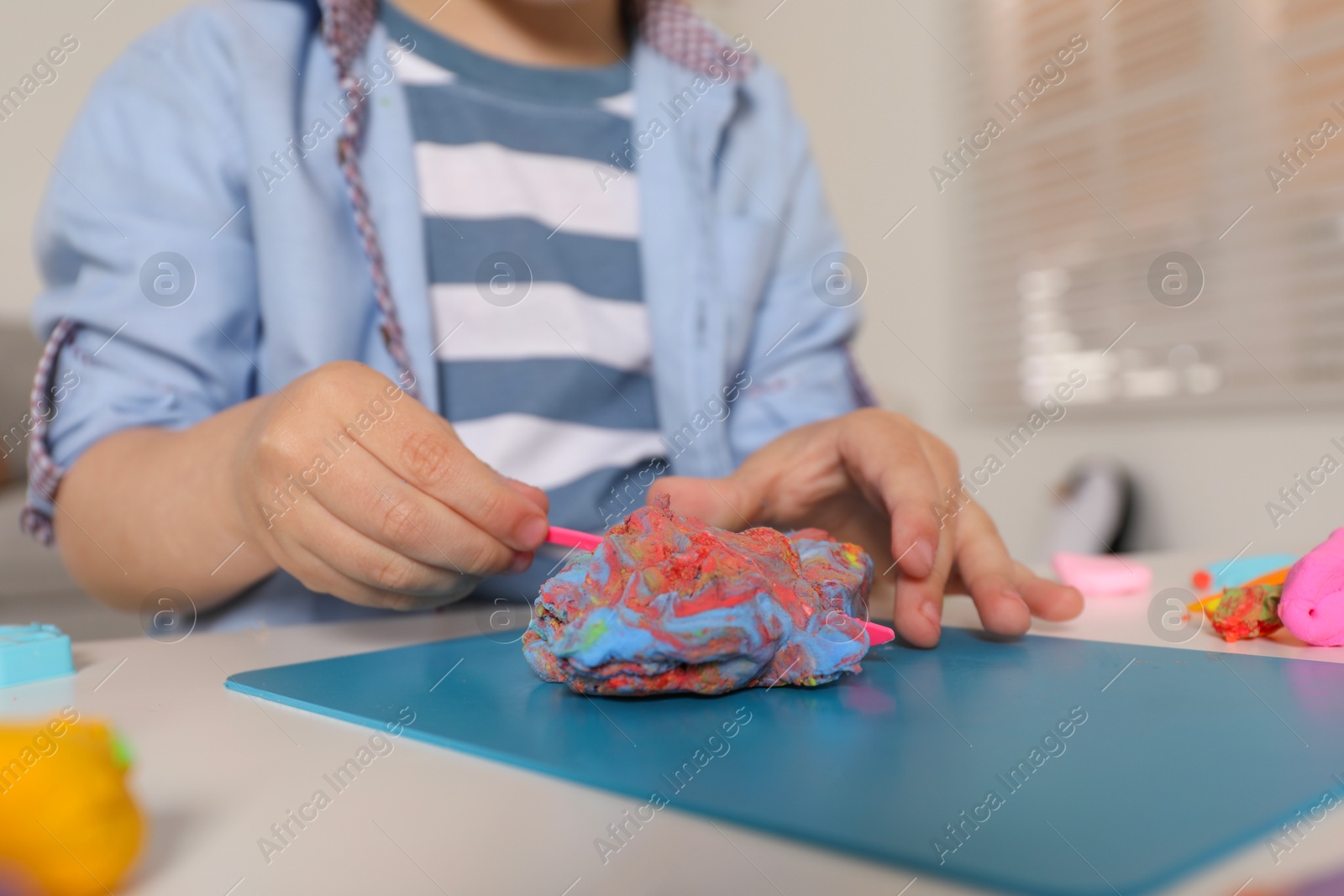 Photo of Little boy sculpting with play dough at table indoors, closeup