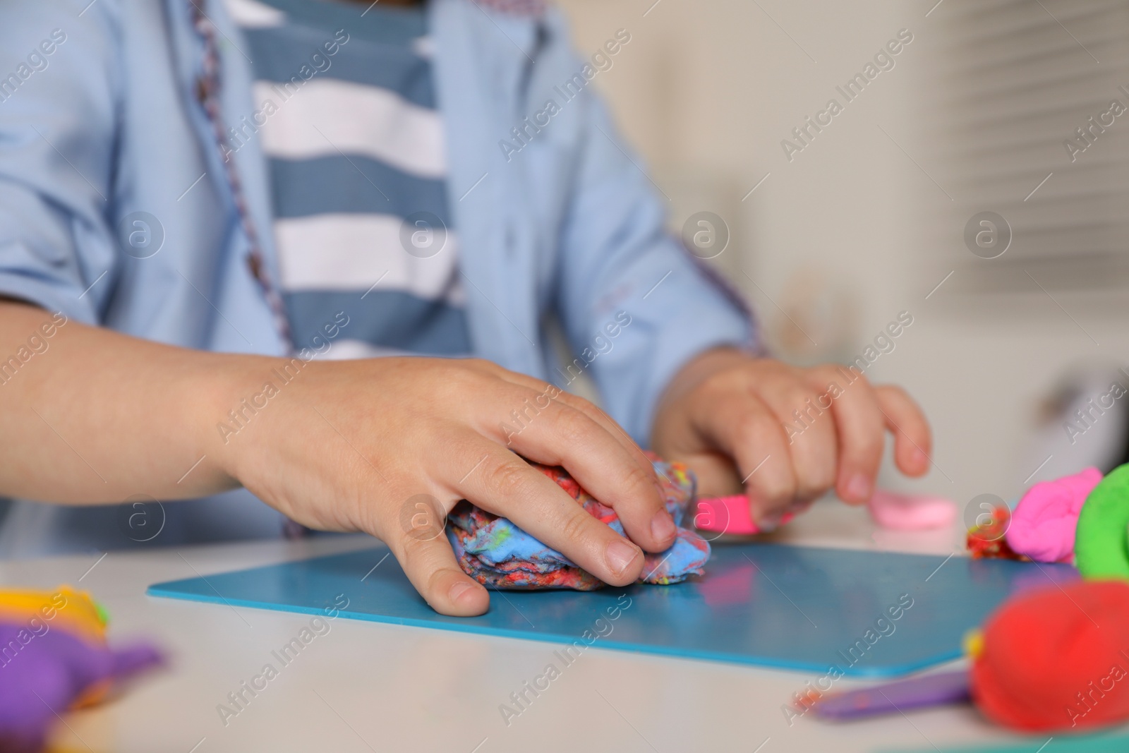 Photo of Little boy sculpting with play dough at table indoors, closeup