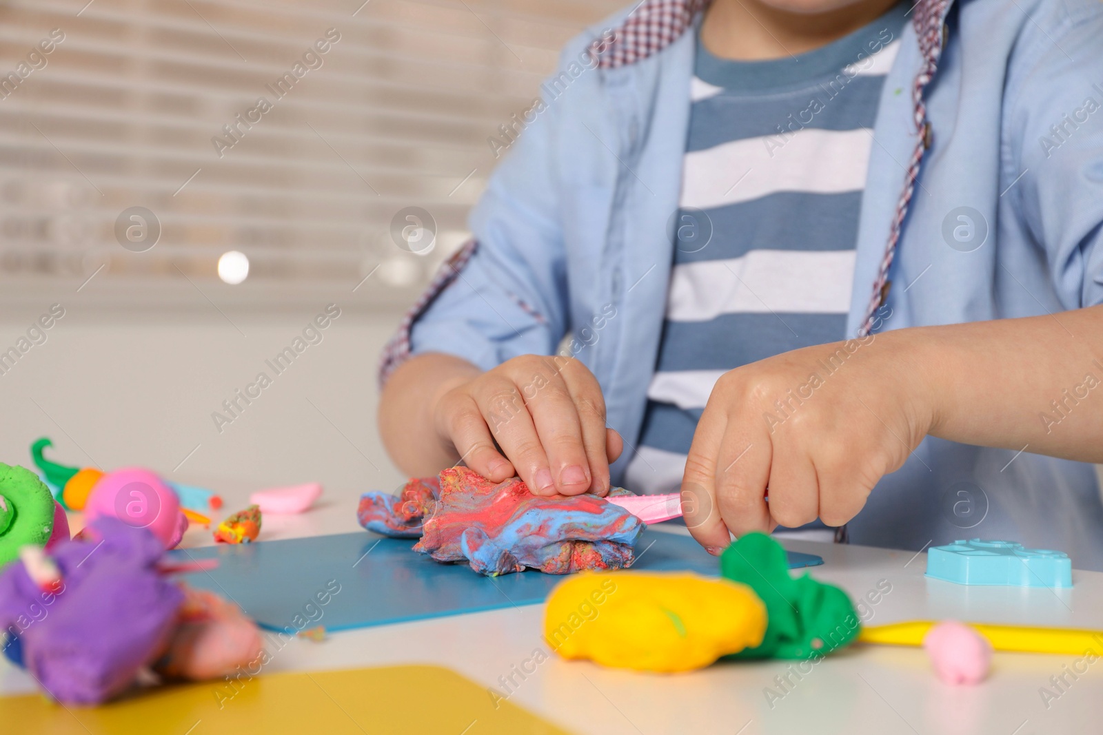 Photo of Little boy sculpting with play dough at table indoors, closeup