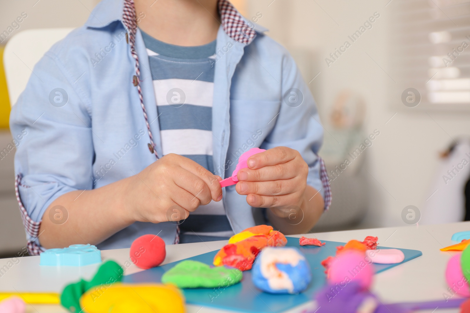 Photo of Little boy sculpting with play dough at table indoors, closeup