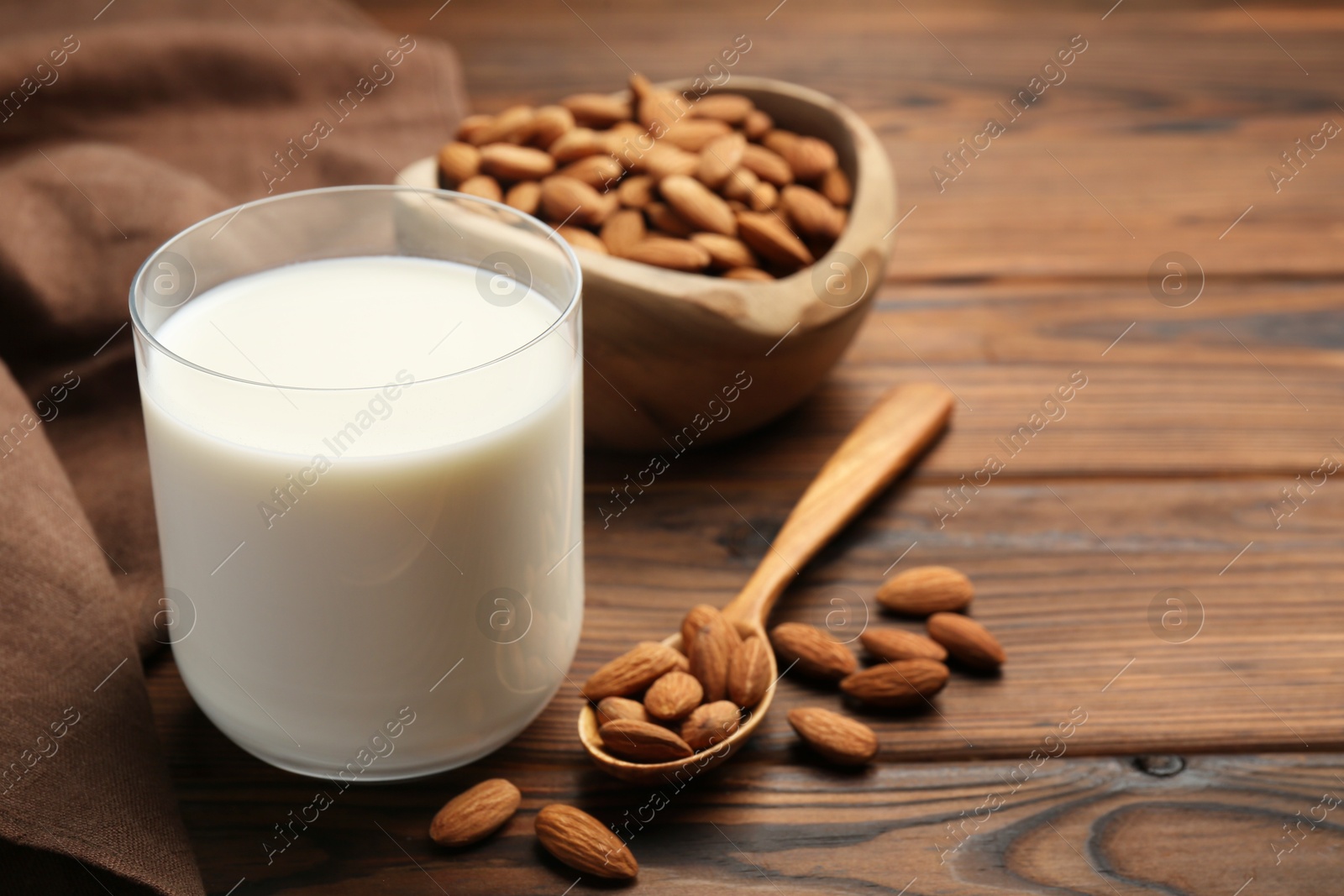 Photo of Glass of almond milk and almonds on wooden table, space for text