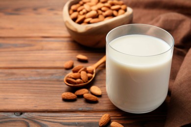 Photo of Glass of almond milk and almonds on wooden table, space for text