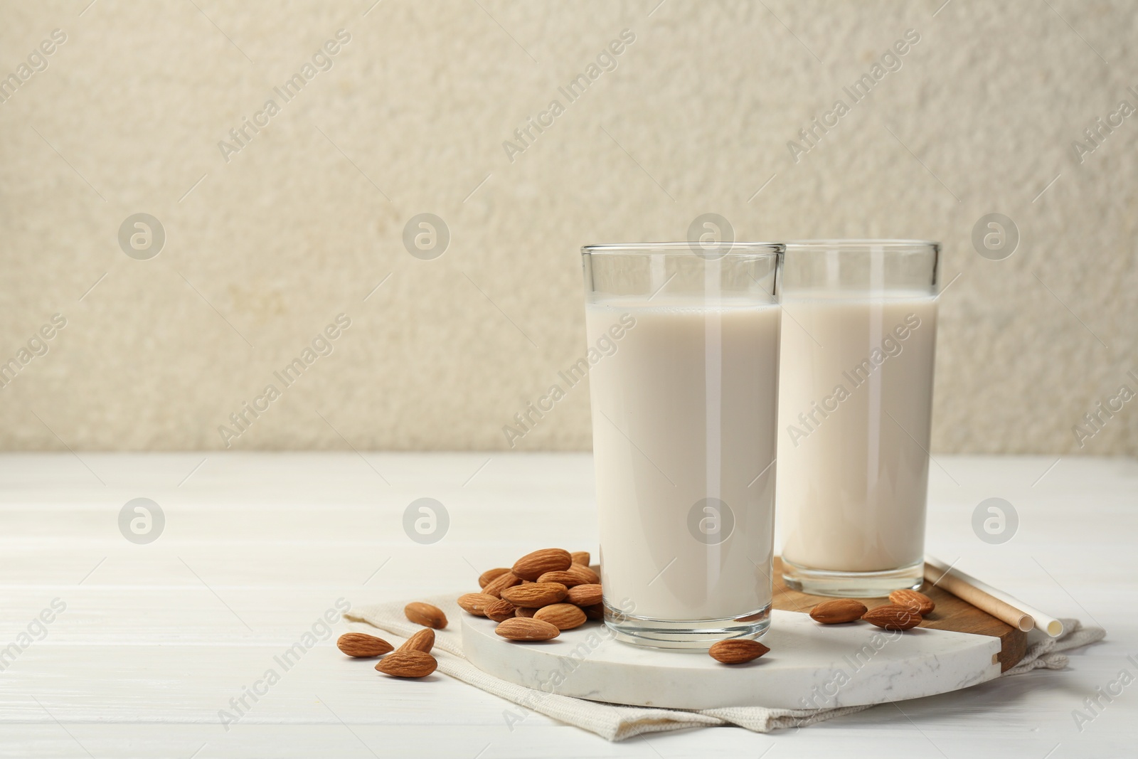 Photo of Glasses of almond milk and almonds on white wooden table, space for text