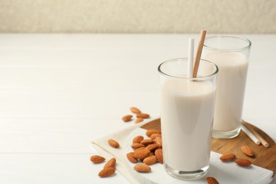 Photo of Glasses of almond milk and almonds on white wooden table, space for text