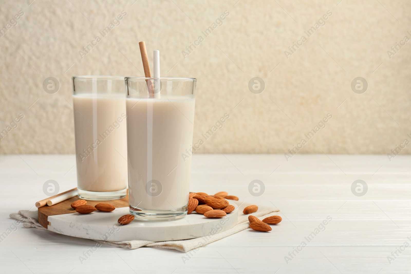 Photo of Glasses of almond milk and almonds on white wooden table, space for text